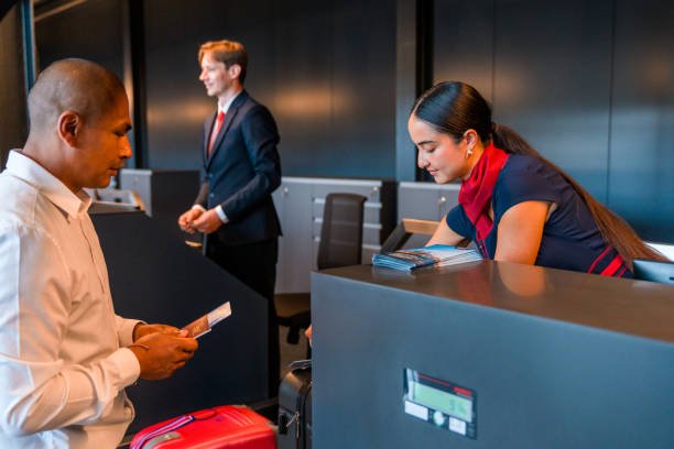 Young adult Asian airline stewardess sitting at a check in counter at the airport checking boarding passes.